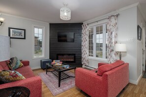 A living room with a fireplace, red sofas, a TV, and a chandelier.