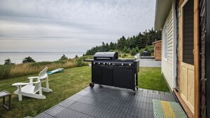 A deck with a grill, a white chair, and a view of the water.