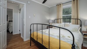 A bedroom with a bed, a ceiling fan, a window with curtains, and a nightstand with a lamp.