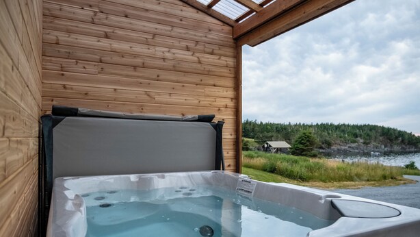 A wooden cabin with a hot tub and a view of a forested area.