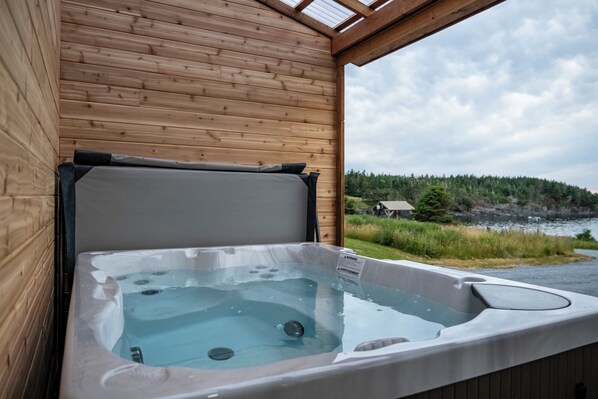 Une cabane en bois avec un jacuzzi et une vue sur une zone boisée.