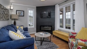 A living room with a blue sofa, a yellow armchair, a fireplace, and a large window.