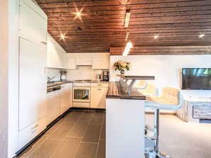 Une cuisine moderne avec des meubles blancs, un four encastré et un coin repas comprenant une table en bois et un canapé.