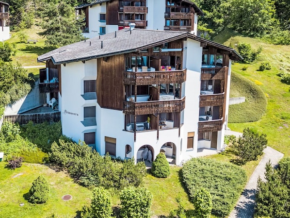 A multi-story building with balconies, a covered outdoor seating area, and a surrounding landscaped garden.