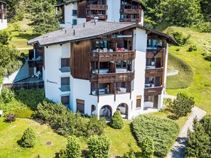 Un immeuble à plusieurs étages doté de balcons, d’un espace extérieur aménagé et couvert pour s’asseoir, et d’un jardin paysager qui l’entoure.