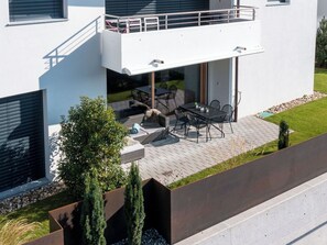 Una moderna casa a due piani con un balcone, un'area salotto esterna e un piccolo giardino.