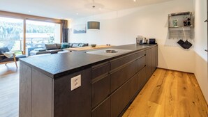 A modern kitchen with a central island, wooden flooring, and a view of the outdoors. - Nice apartment for 6 guests with WIFI, TV, patio and panoramic view (Waldhaus)