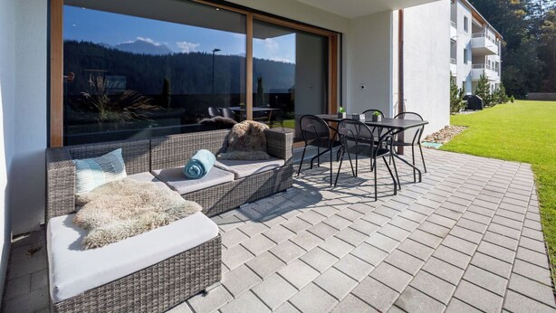 A modern outdoor seating area with wicker furniture and a glass door leading to a view of a mountain landscape. - Nice apartment for 6 guests with WIFI, TV, patio and panoramic view (Waldhaus)