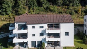 A multi-story residential building with balconies, a covered outdoor seating area, and a view of a natural landscape. - Nice apartment for 6 guests with WIFI, TV, patio and panoramic view (Waldhaus)