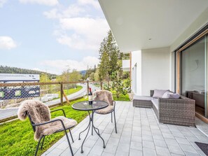 Un balcone con tavolo e sedie, un divano e vista su una strada e del verde.