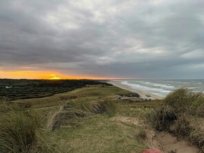 Eine Küstenlandschaft mit Sonnenuntergang, Wiesen und einem Strand.