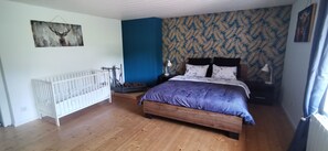 A bedroom with a wooden floor, a white crib, a bed with a purple bedspread, a nightstand with a lamp, and a wall with a leaf-patterned wallpaper. - Renovated farmhouse from 1791 with a hot tub; pets welcome; near Alsace (Provenchères-et-Colroy)