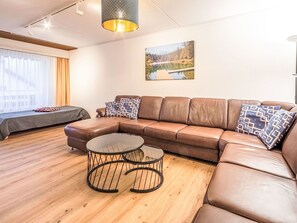 Ein modernes Wohnzimmer mit einer braunen Ledersofa, einem Glastisch und einem Gemälde einer Seenlandschaft an der Wand.