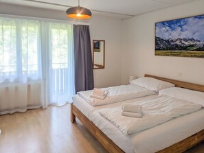 Ein Hotelzimmer mit einem Bett, einem Fenster mit transparenten Vorhängen, einem Gemälde an der Wand und einer Pendelleuchte.