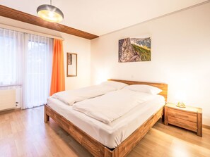 Ein Schlafzimmer mit einem hölzernen Bett, einem Nachttisch, einer Lampe, einem Fenster mit Vorhängen und einem Gemälde an der Wand.