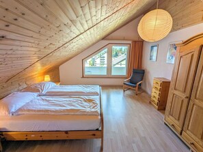 Ein Schlafzimmer mit schrägverdeckter Decke, einem Bett, einem Sessel und einem Kleiderschrank.