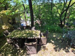 Eine Terrasse mit Tisch und Stühlen, umgeben von Bäumen und einem Zaun.