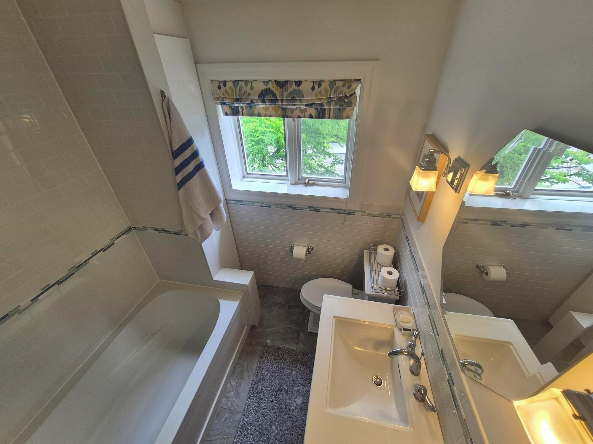 A bathroom with a bathtub, a sink, a toilet, and a window with a view of greenery.