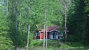 Une petite cabane rouge, entourée d’une forêt dense.