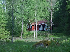 Eine kleine, rote Holzhütte, umgeben von dichtem Wald.