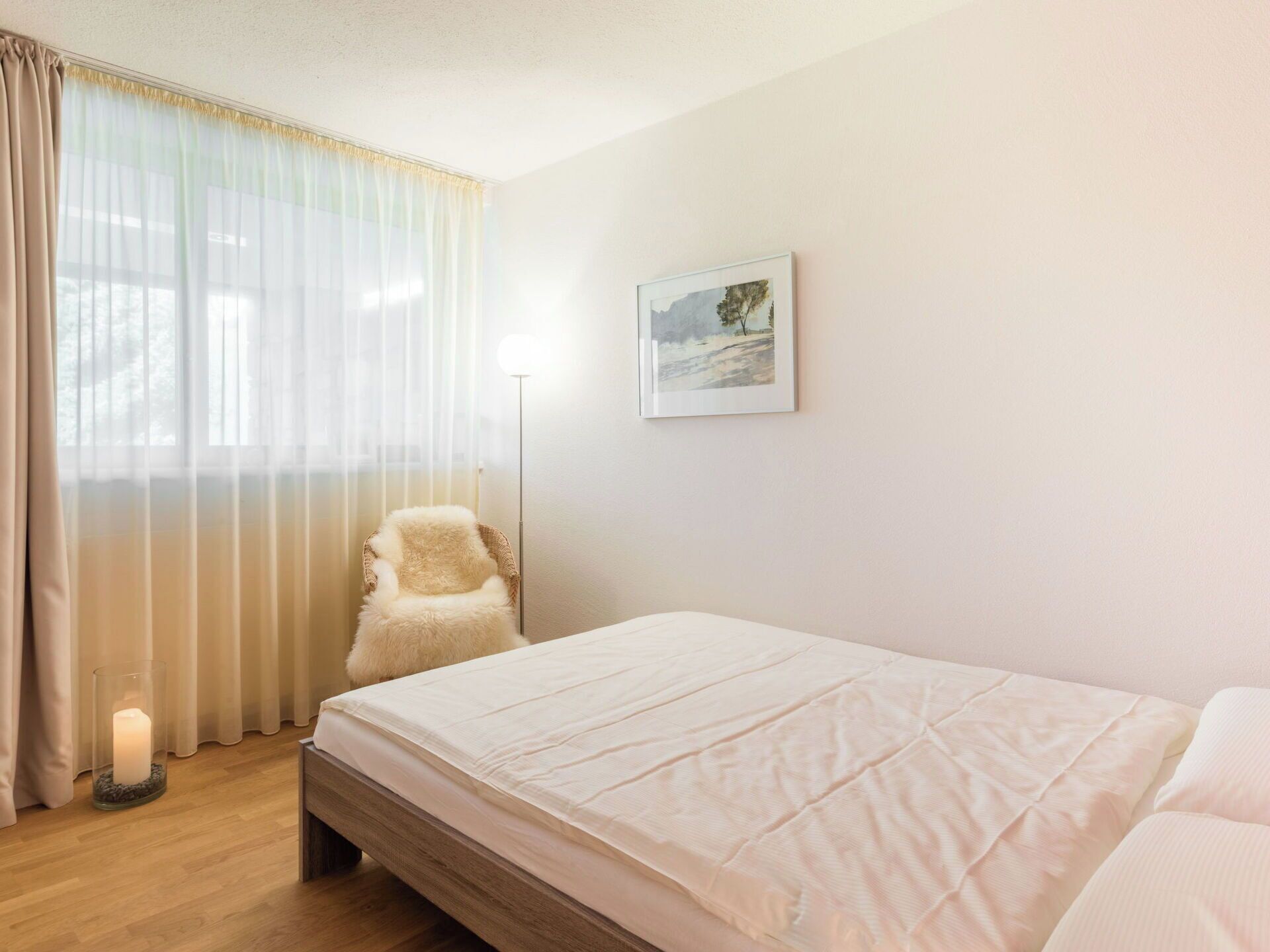 Een slaapkamer met een bed, een stoel, een vloerlamp en een schilderij aan de muur.