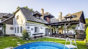 Ett hus med en swimmingpool, en täckt uteplats och en eldstad i sten.