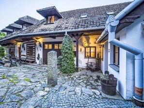 A traditional chalet with a stone courtyard, wooden exterior, and a small Christmas tree.