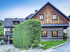 A wooden cabin with a stone foundation, a balcony, and a well-maintained lawn.