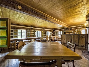 A rustic wooden interior with a large dining table, benches, and a bar area.