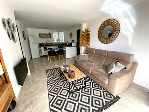 A modern living room with a sofa, coffee table, and patterned rug. A kitchen is visible in the background with a dining area. - "Le Trinité" near beach and port (La Ciotat)