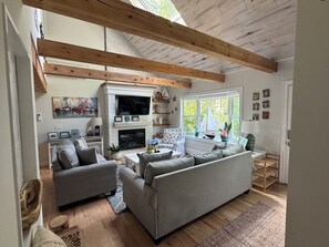 En stue med pejs, sofaer, fjernsyn og et vindue med en modelsejlbåd.