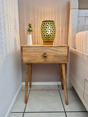 Ein Nachttisch aus Holz mit einer Schublade, eine dekorative Lampe mit geometrischem Muster und eine kleine Pflanze.