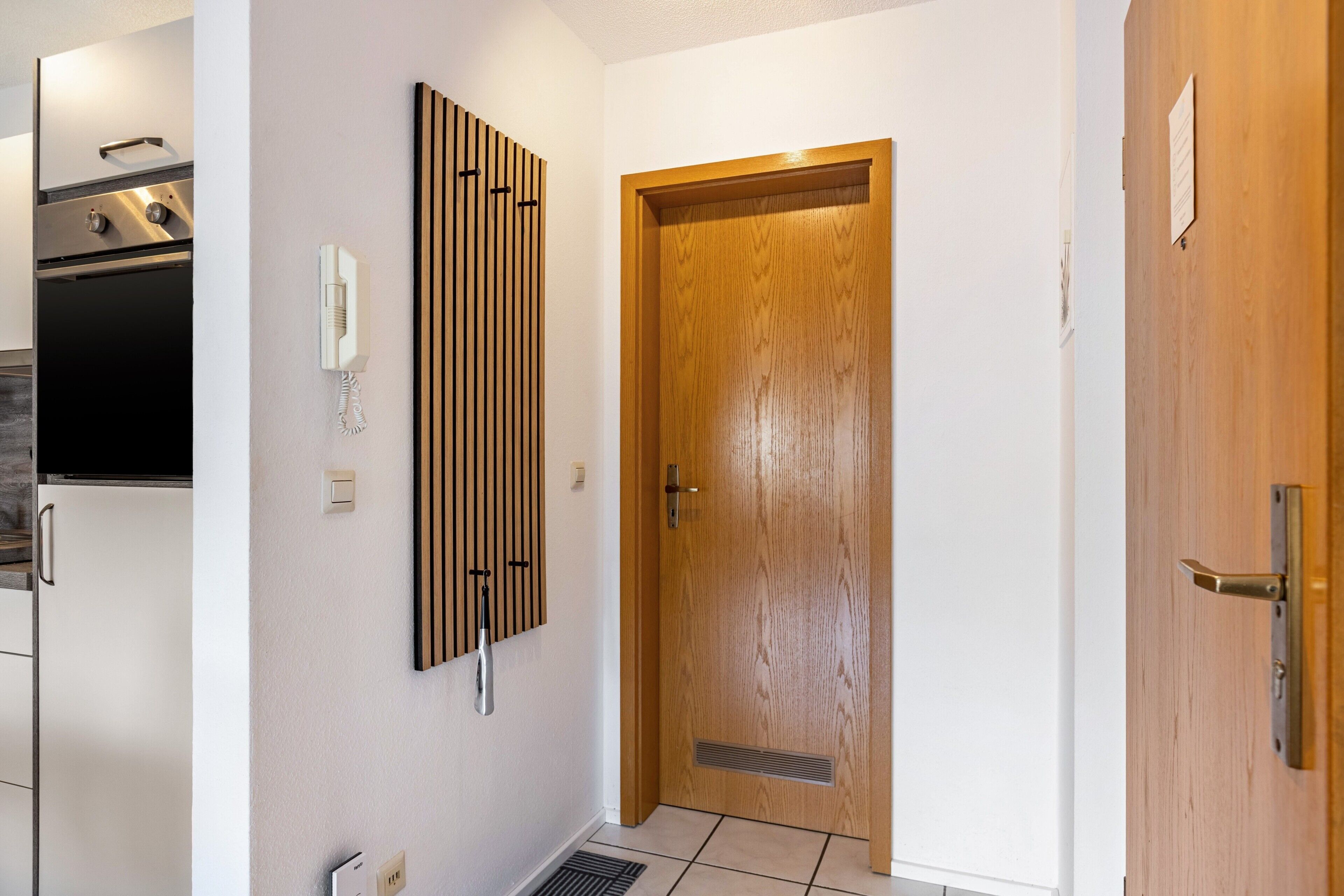 Une cuisine équipée d’un four encastré, d’un téléphone fixé au mur et d’une porte en bois dotée d’un judas.