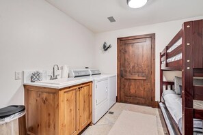 A compact room with a wooden cabinet, a washing machine, a dryer, a bunk bed, and a door. - Private Ski-out Village Home in Vail with Hot Tub (Vail)