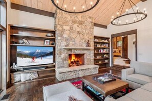 A living room with a stone fireplace, a television, bookshelves, and a sofa. - Private Ski-out Village Home in Vail with Hot Tub (Vail)