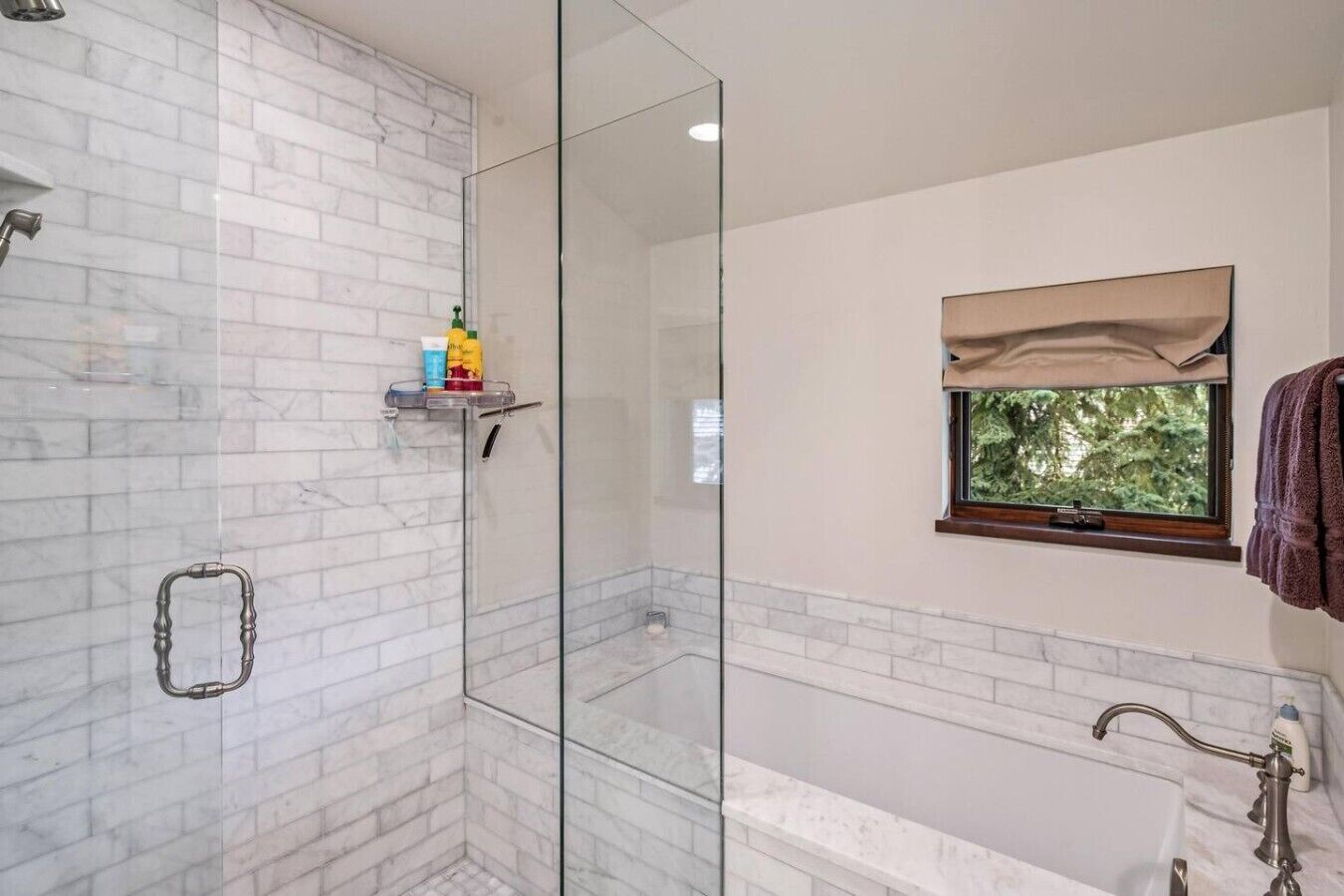 Ein modernes Badezimmer mit Duschkabine aus Glas, einer Badewanne und einem Fenster mit Blick auf Bäume.