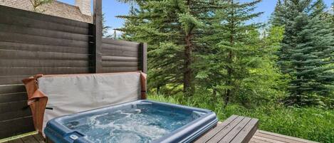 A hot tub on a wooden deck with a wooden fence and trees in the background.