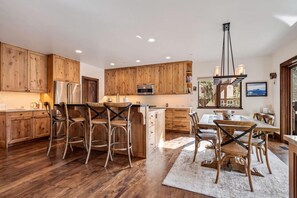 A kitchen with wooden cabinets, a dining area with a table and chairs, and a view of the outdoors through a window. - Private Ski-out Village Home in Vail with Hot Tub (Vail)