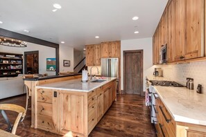 A modern kitchen with wooden cabinetry, a central island, stainless steel appliances, and a built-in oven. - Private Ski-out Village Home in Vail with Hot Tub (Vail)