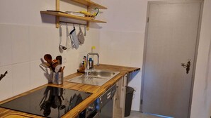 A compact kitchen with a wooden countertop, stainless steel sink, and a dishwasher. There are hanging utensils and a small shelf above the sink. - Cozy attic apartment with garden access (Burg Stargard)