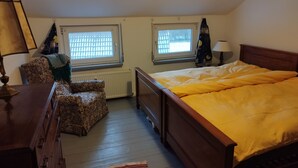 A bedroom with a wooden bed, two windows, a radiator, a chair, and a dresser. - Cozy attic apartment with garden access (Burg Stargard)
