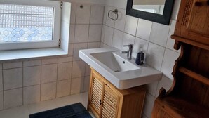 A bathroom with a window, a sink, a mirror, and wooden cabinets. - Cozy attic apartment with garden access (Burg Stargard)