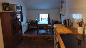 A compact kitchen with a microwave, stove, and wooden table. - Cozy attic apartment with garden access (Burg Stargard)