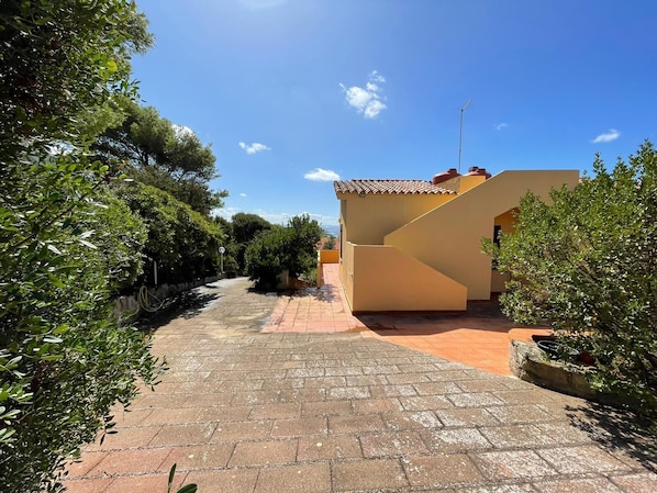 A paved pathway leading to a building with a tiled roof and a satellite dish. - Rent small villa with large garden equipped with all amenities. (Torre dei Corsari)