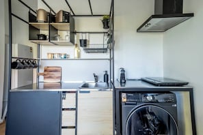 Una cocina compacta con lavadora, cafetera y un ordenador portátil sobre la encimera.