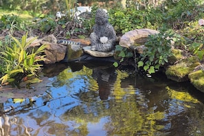 A serene garden with a pond, a stone statue, and lush greenery.