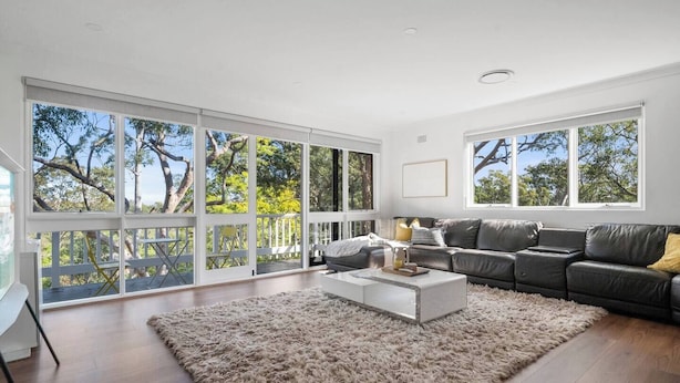 A spacious living room with large windows, a dark leather sofa, a white coffee table, and a fluffy rug. - Warrina Natural Serenity meets City Energy (Chatswood West)