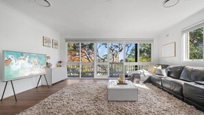 A spacious living room with a large window, a gray sofa, a coffee table, and a painting on the wall. - Warrina Natural Serenity meets City Energy (Chatswood West)