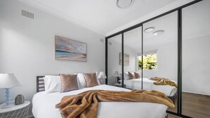 A modern hotel room with a large bed, a bedside table with a lamp, a mirror, and a painting on the wall. - Warrina Natural Serenity meets City Energy (Chatswood West)