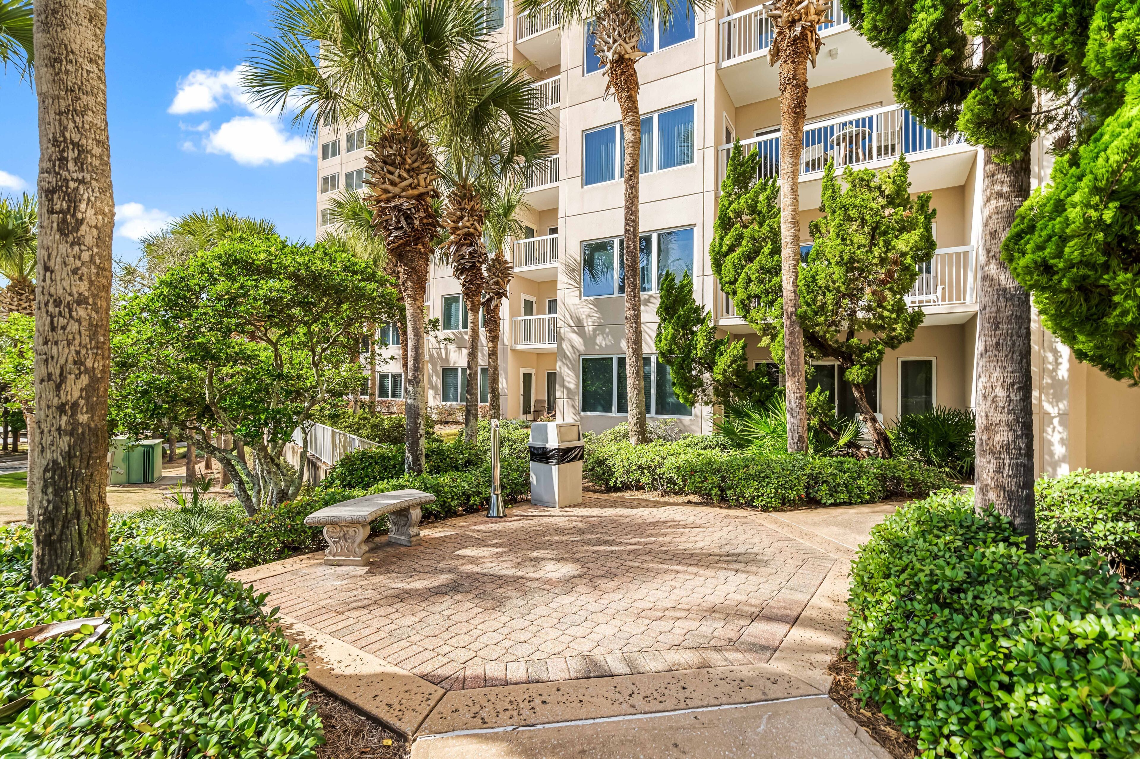 A courtyard with palm trees, a bench, and a building with balconies.